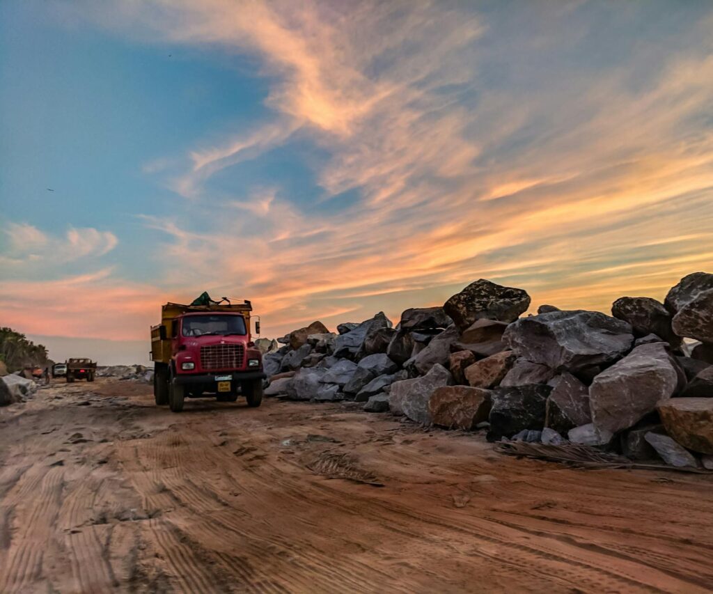 red dump truck near filed rocks under cloudy sky