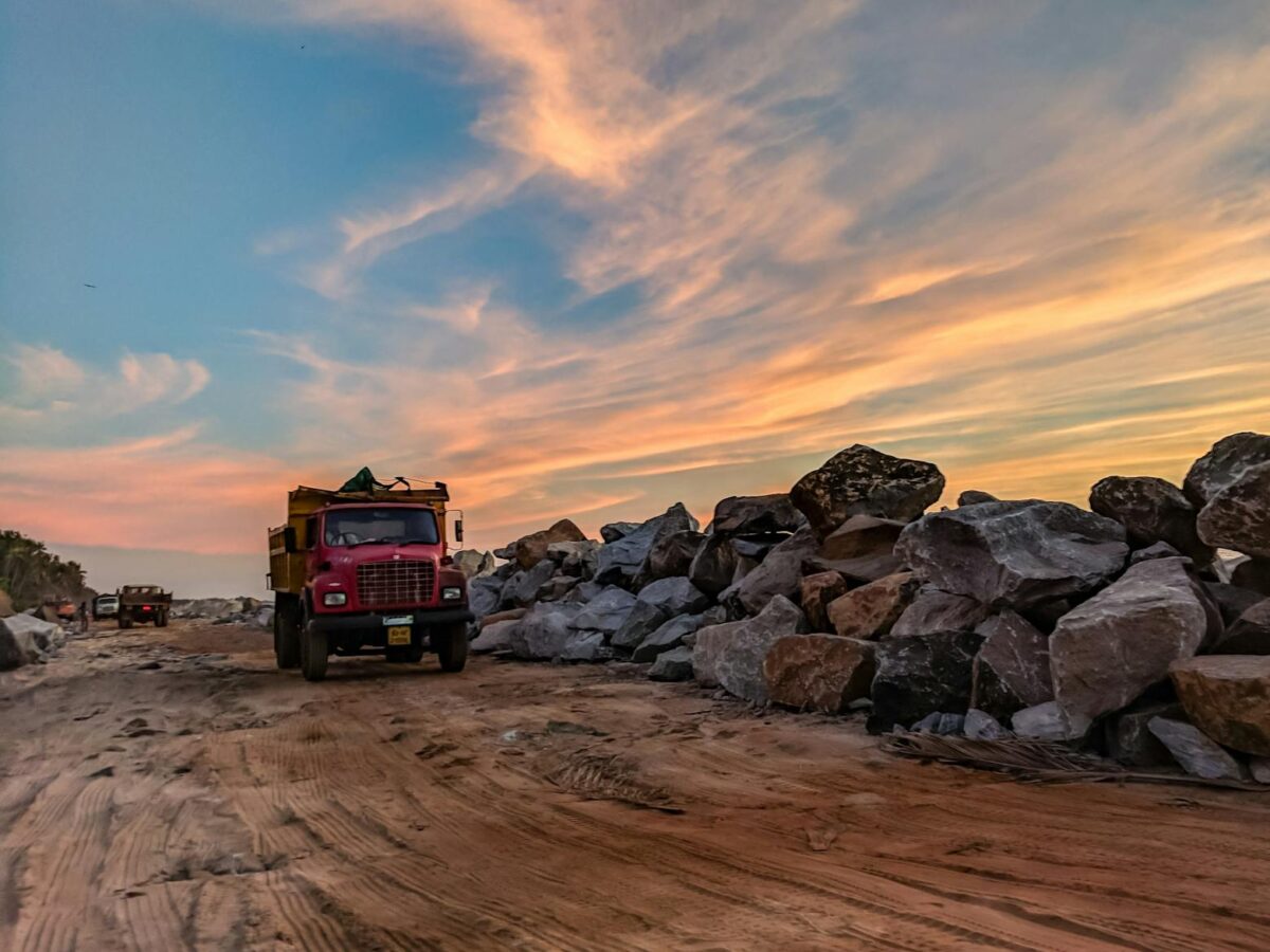 red dump truck near filed rocks under cloudy sky