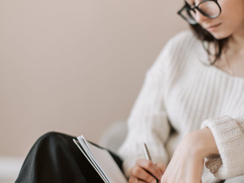 crop young woman writing schedule in diary on sofa