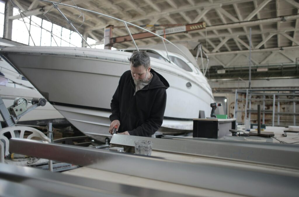 bearded mechanic working with metal part near boat