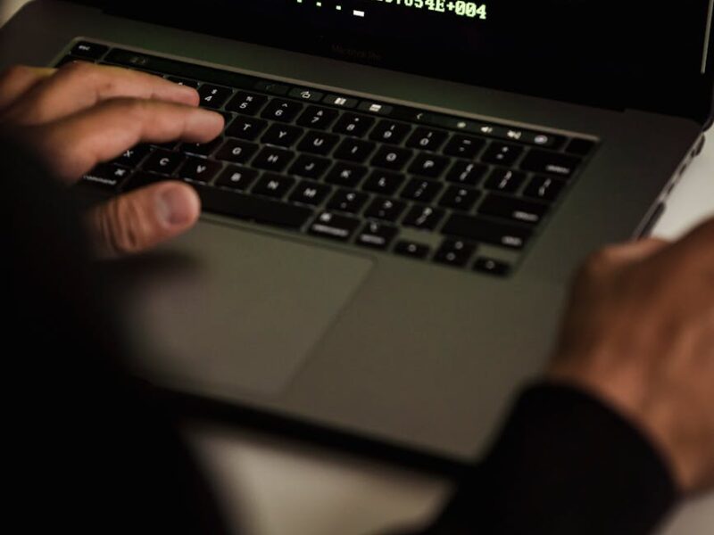 crop hacker typing on laptop with data on screen