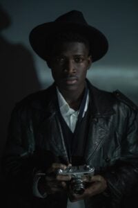 a man wearing a leather jacket holding an analog camera