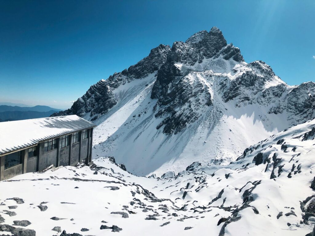 a snow covered mountain near the wooden house under the blue sky