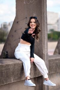 a woman in white pants and crop top sitting on a ledge