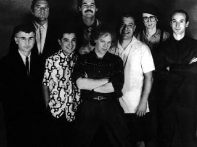 27 March 1987, OINGO BOINGO , (left to right) Dale Turner, Sam Phipps, John Avila, Steve Bartek, Danny Elfman, Johnny "Vatos" Hernandez, Mike Bacich, Leon Schneiderman , MCA Records, Public domain, via Wikimedia Commons